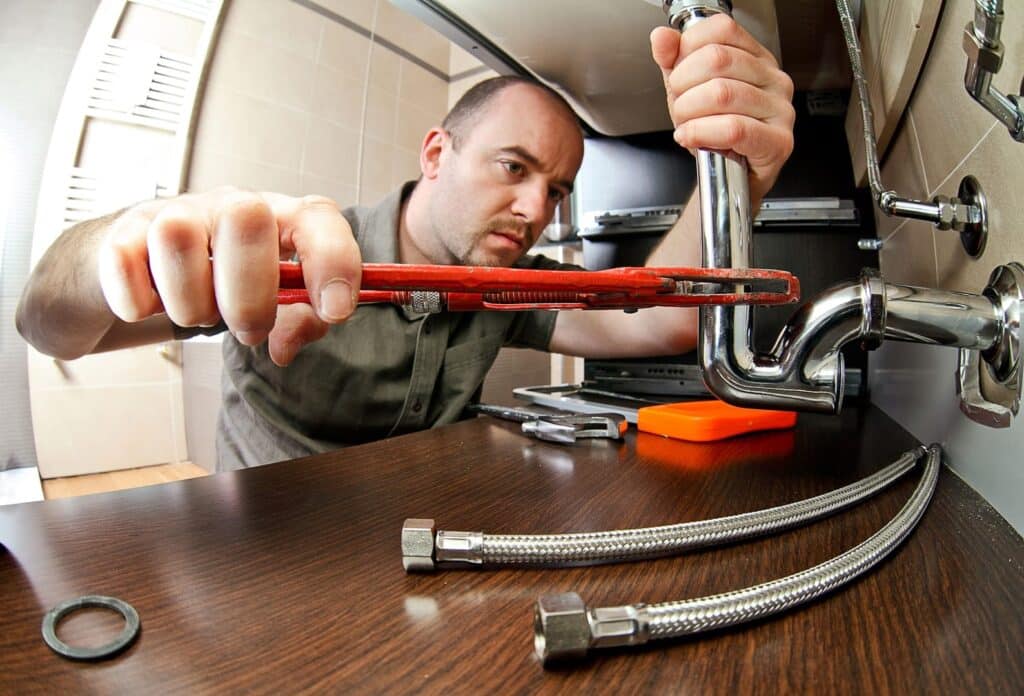 plumber installing a sewer line cleanout by tightening pipes with a pipe wrench