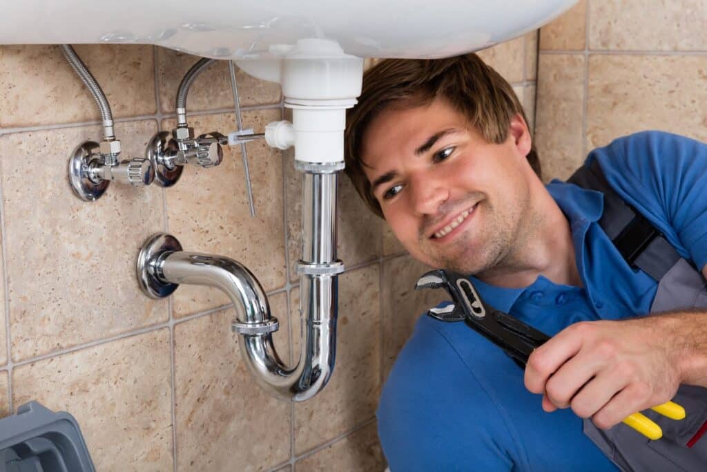 A plumber using a wrench to perform a professional sink repair on a chrome P-trap and drain line under a bathroom sink